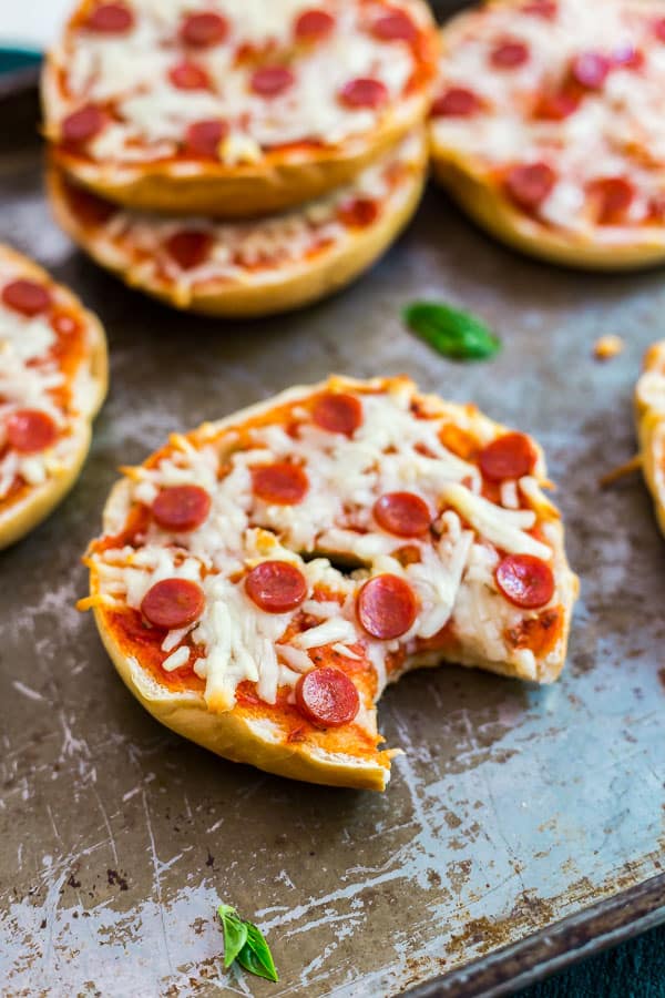 A Freezer Friendly Pizza Bagel with a bite out of it on a pan with other pizza bagels behind it.