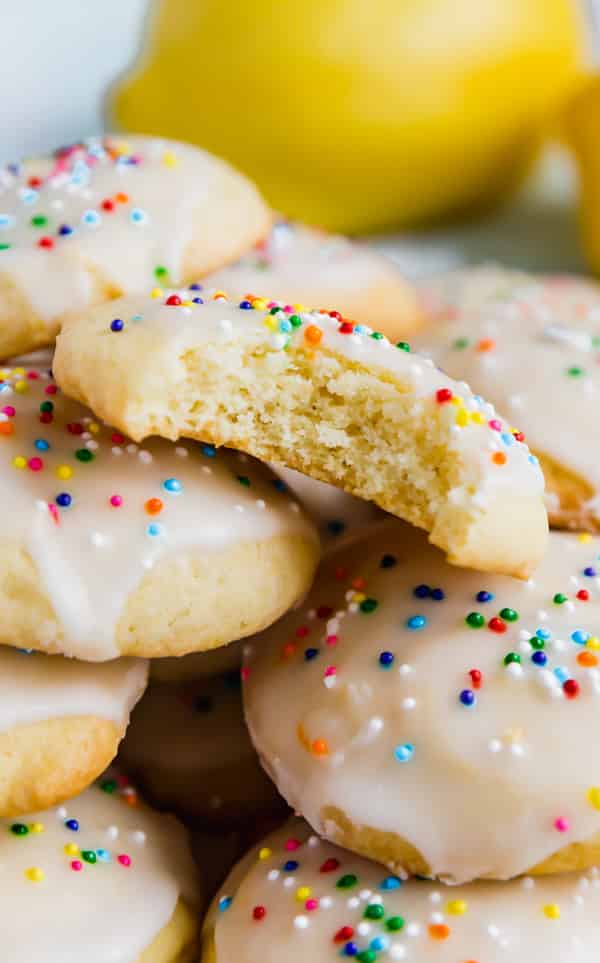 A close up shot of sour cream cookies with a bite out of one exposing the cakey-interior