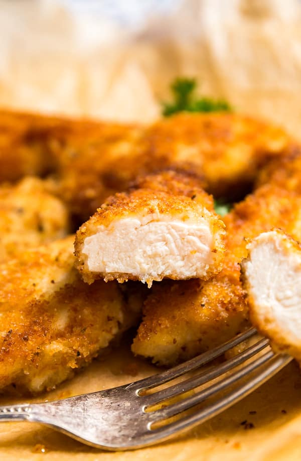 A chicken cutlet cut in half revealing the cooked inside positioned on top of other chicken cutlets.