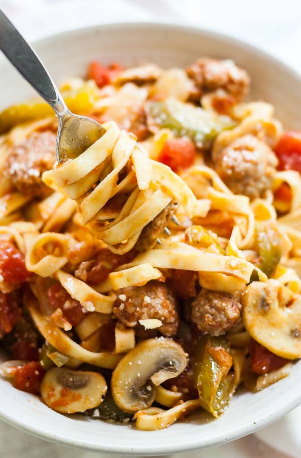 A clost up shot of a fork twisting some Sausage and peppers pasta.