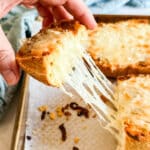 A hand pulling up a piece of garlic cheesy bread trailing melted cheese.