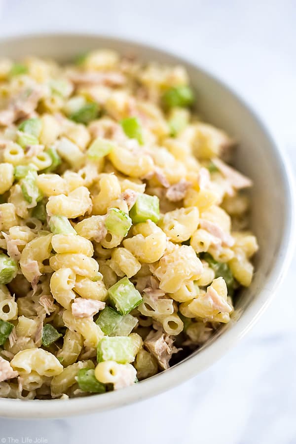 A closeup image of the side of a bowl of mac salad with tuna, celery and onions in it with elbow pasta.