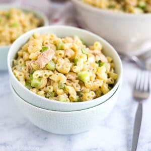 A square image of a bowl of tuna macaroni salad stacked on a second white bowl with a fork next to it and more mac salad in the background.