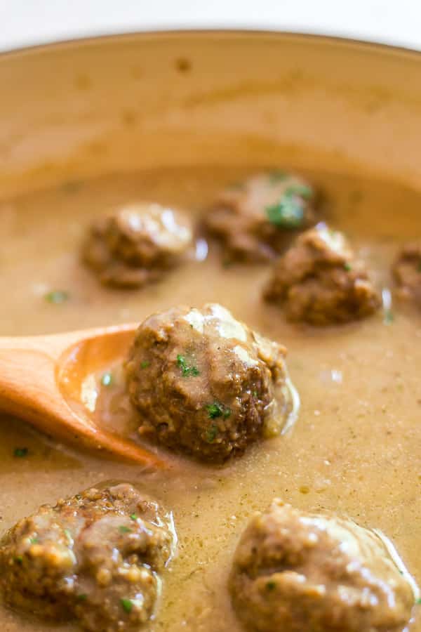 One of the Classic Swedish Meatballs on a spoon in a pan containing other Classic Swedish Meatballs.