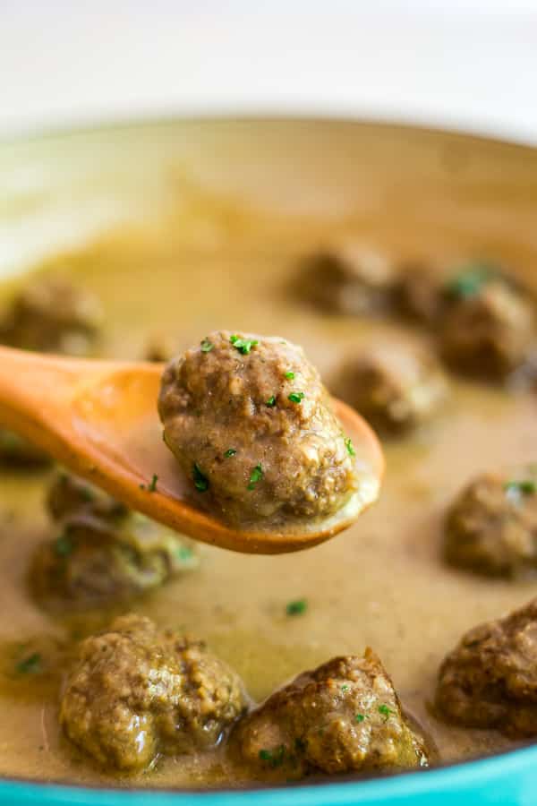A wooden spoon lifting up one of the Classic Swedish Meatballs with other meatballs in the background.