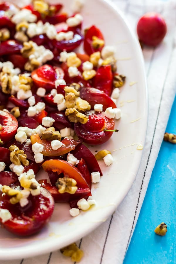 The side of a plate of plums with goat cheese and walnuts/
