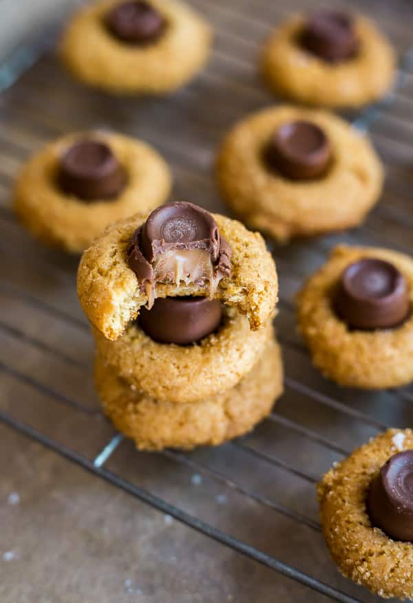 Salted Caramel Blossoms Cookies on a cooling rack with a stack of them in the front anda bite taken out of the top one.