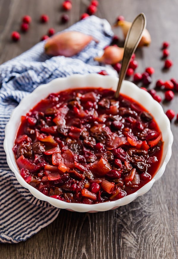 Homemade Cranberry Sauce with Dried Cherries and Shallots in a white bowl with fresh cranberries surrounding it.