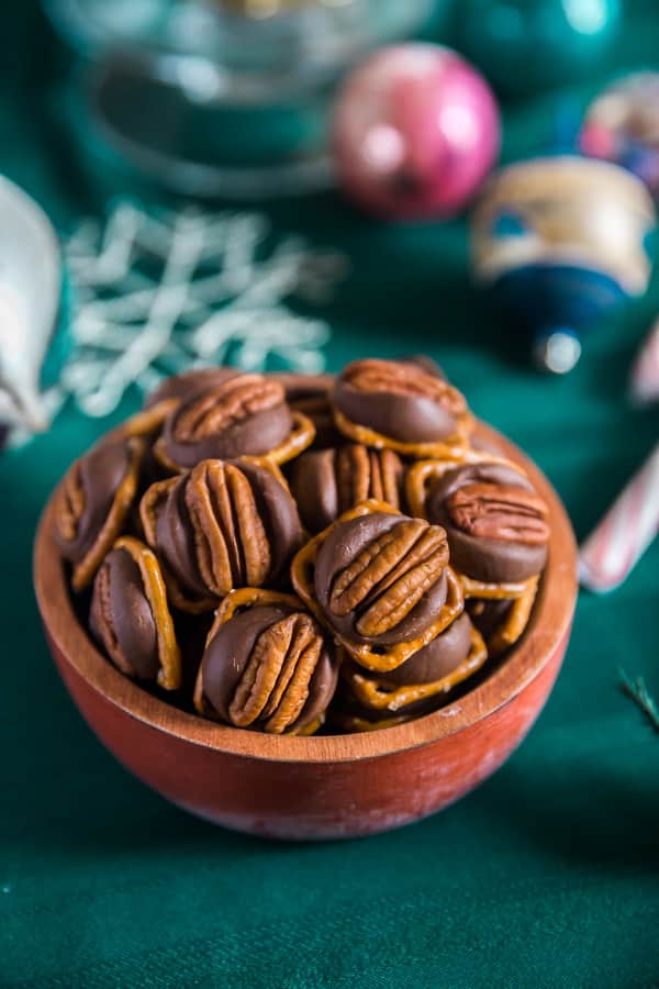 A bowl of Chocolate Caramel Pretzel Turtles with ornaments in the background.