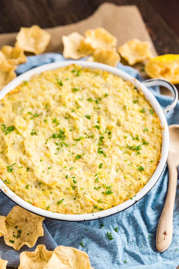 A pan of Hot Artichoke Dip with chips around it.