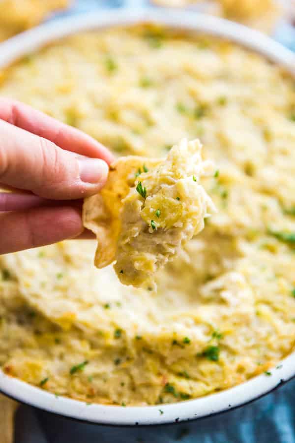 A hand holding up a chop with Hot Artichoke Dip on it.