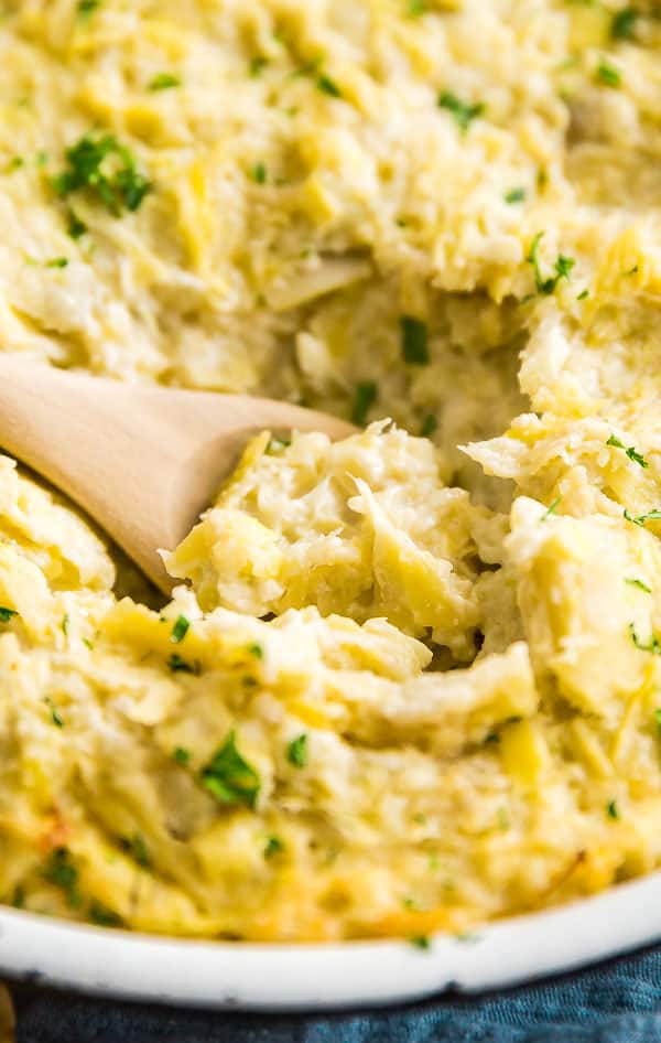 A close up photo of Hot Artichoke Dip with a spoon in it.