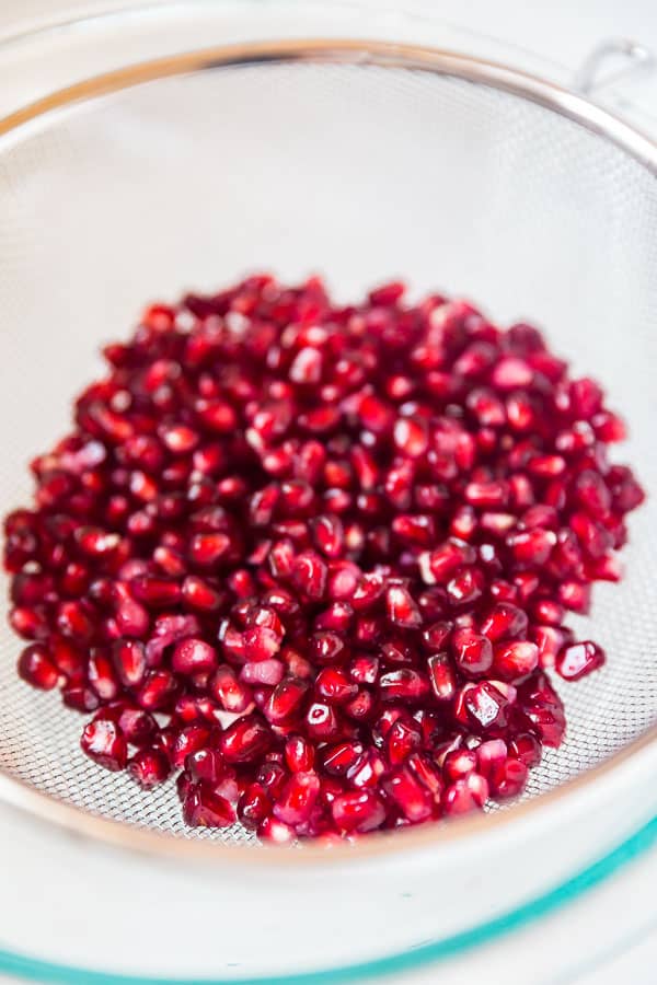 Pomegranate seeds draining in a strainer for How to peel a pomegranate.