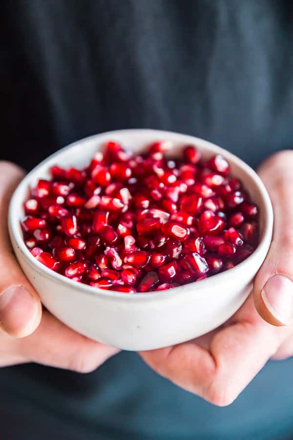 Hands holding a bowl of pomegranate seeds for How to peel a pomegranate.