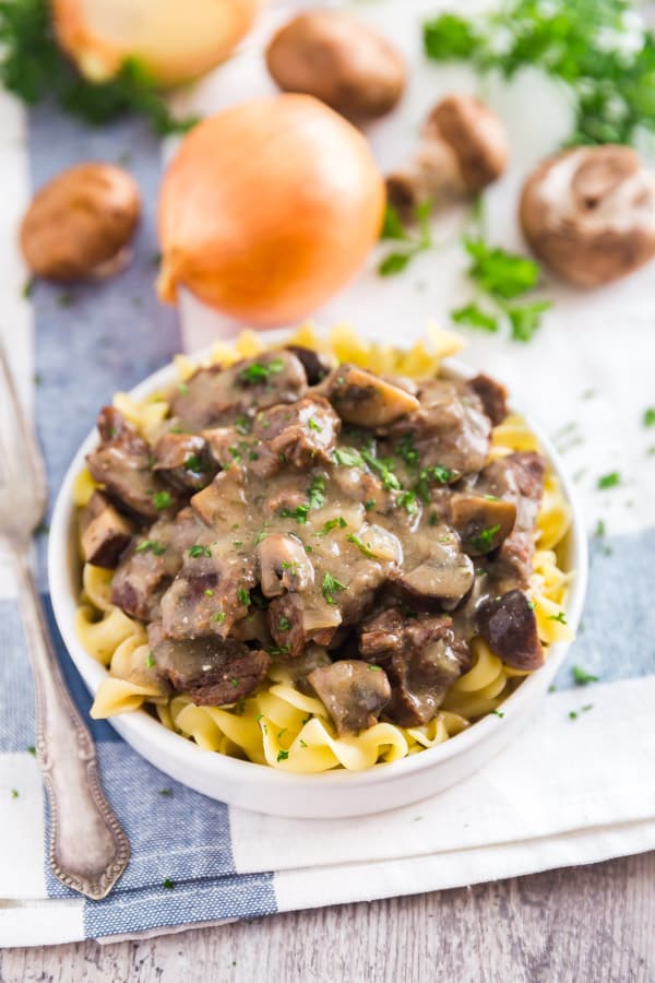 A plate of Easy Beef Stroganoff Recipe with onion and mushrooms behind it.