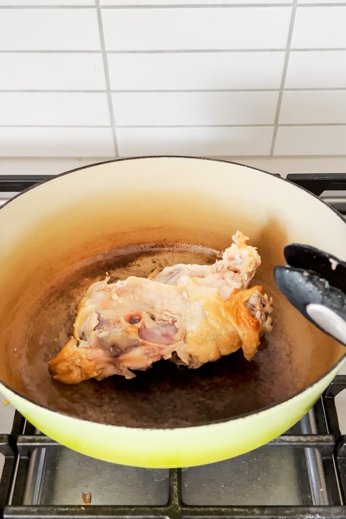 A chicken carcass browning in a dutch oven on the stove.