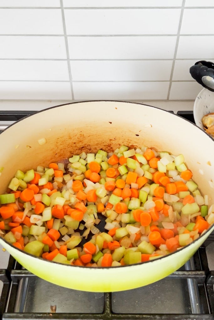 Chopped vegetables caramelizing in a dutch oven on the stove.