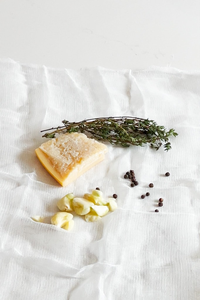 Garlic, peppercorns, fresh herbs and a parmesan rind on top of a cheesecloth.