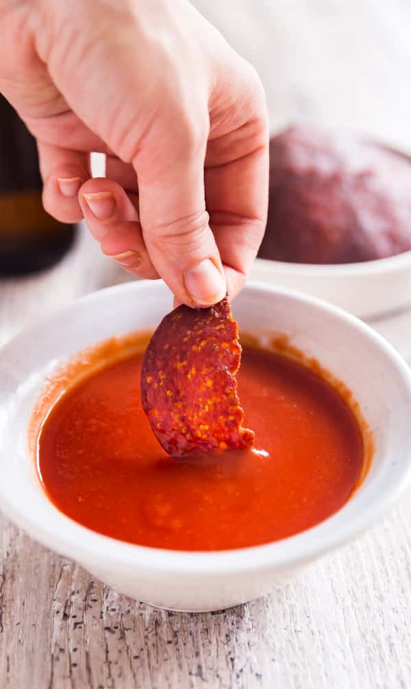 A hand dipping a half a pepperoni chip in to marinara sauce.