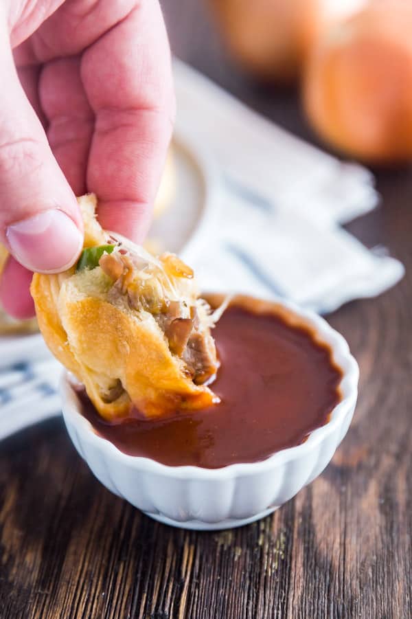 A piece of a Philly Cheese Steak Stuffed Bread Roll being sdipped into a bowl of A1 steak sauce.