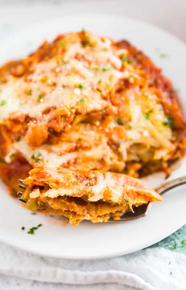 A plate of Baked Eggplant Parmesan with a bite on a fork in the front.