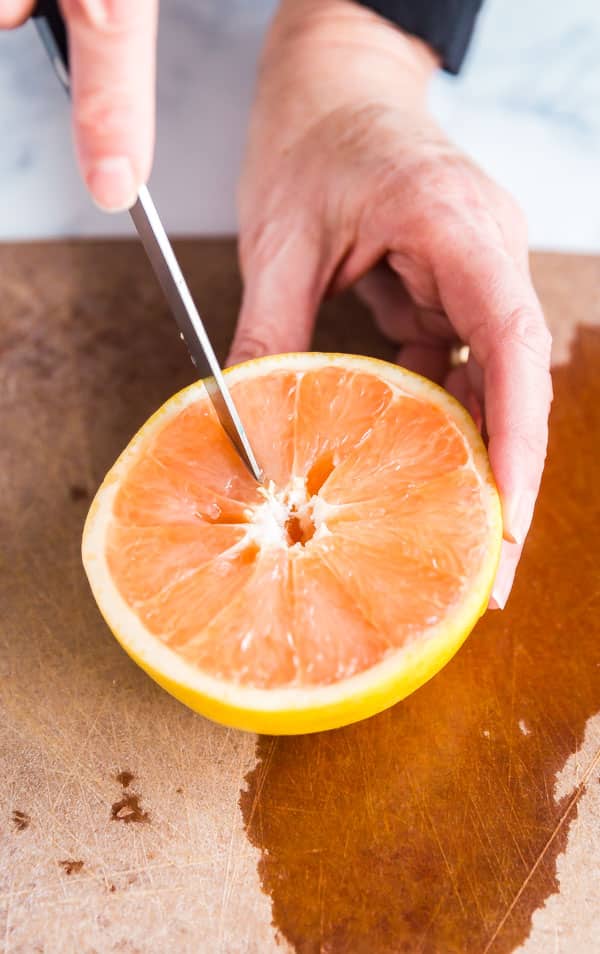 A hand cutting half a grapefruit.