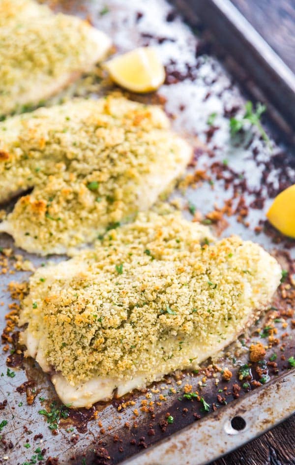 A side shot of Tilapia filets lined up at an angle on a pan with lemons on the side.