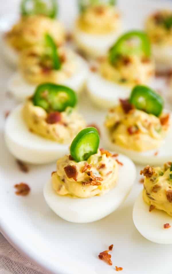 A side shot of deviled eggs topped with jalapeños and bacon. 