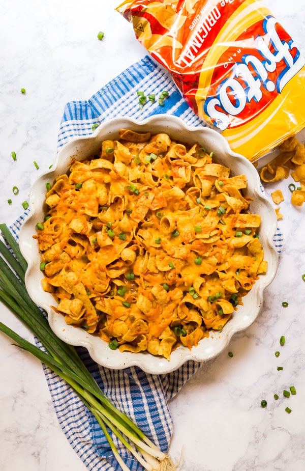 An overhead image of Frito Pie in a pan with scallions around it and a bag of Fritos on the side spilling out.