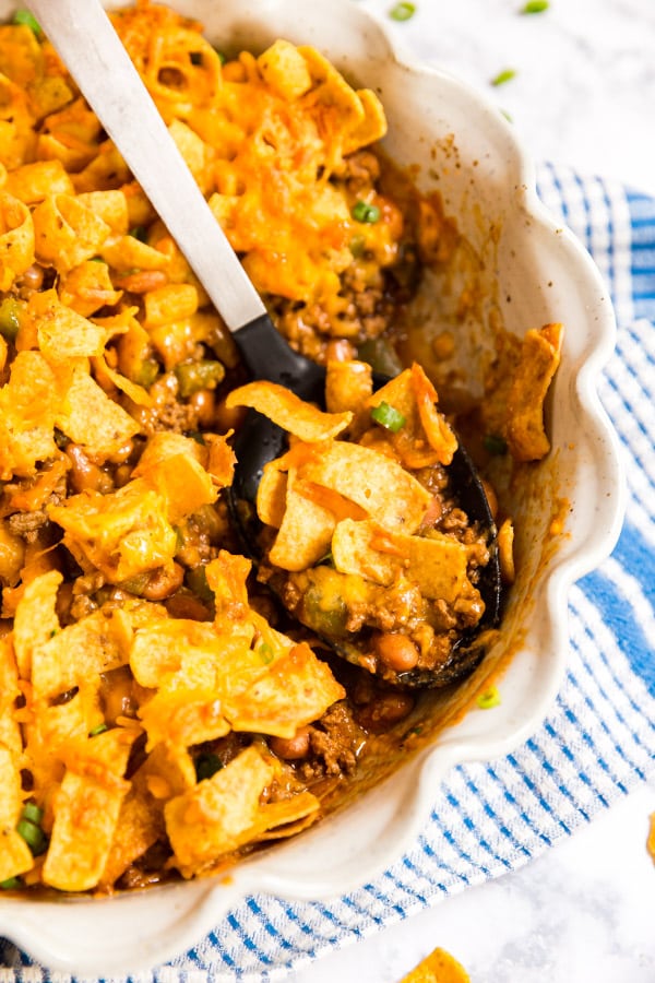 A serving spoon with a scoop of Frito casserole in the pan with the rest of the casserole.