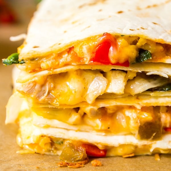 A square close up image of the edge of a stack of quesadilla on top of each other showcasing the gooey cheese and fillings.