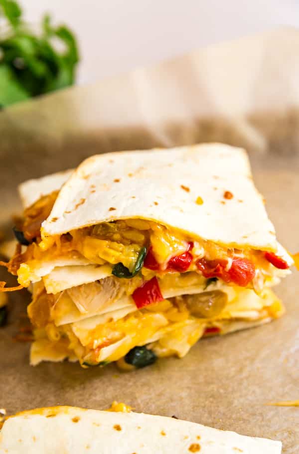 Wedges of quesadilla stacked on top of each other on a pan lined with parchment.