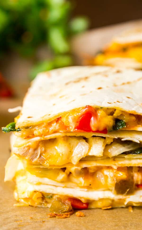 A close up image of the edge of a stack of quesadilla on top of each other showcasing the gooey cheese and fillings.