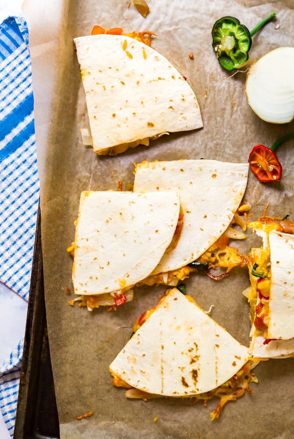 An overhead image of various wedges of chicken quesadillas on a parchment lined pan.