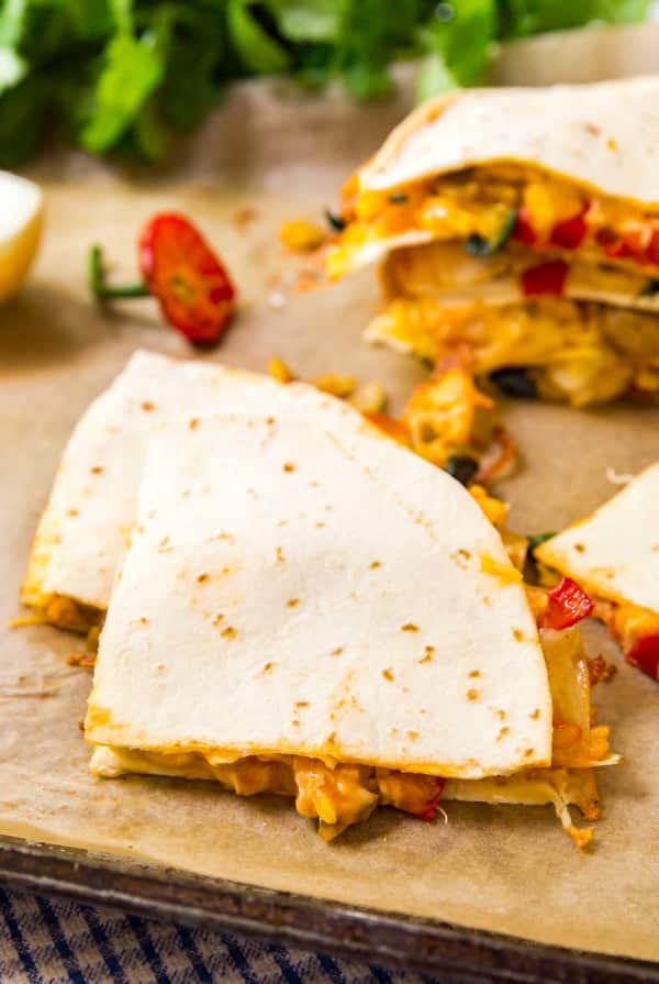 A close up image of a couple wedges of quesadilla on parchment in a pan with other quesadilla wedges in the background.