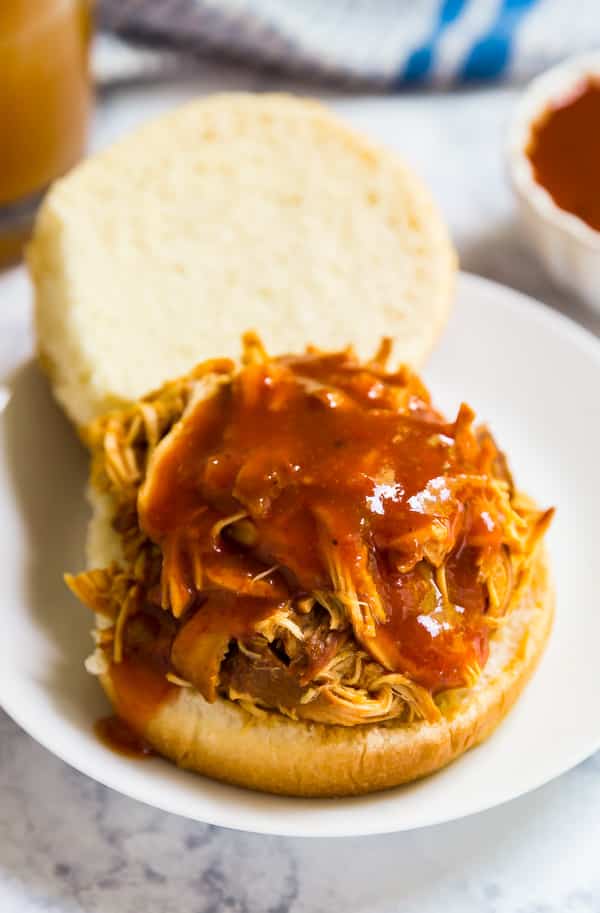 A bun with the top open with shredded bbq chicken and extra barbecue sauce on it.