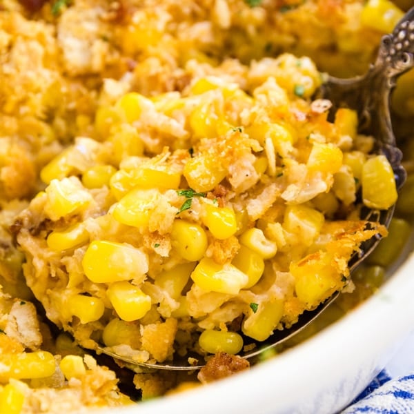 A serving spoon holding a scoop of corn casserole in a baking dish with the rest of the corn casserole behind it.