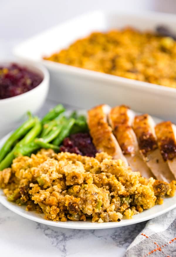 A plate focusing on sausage stuffing with turkey and green beans in the background of it.