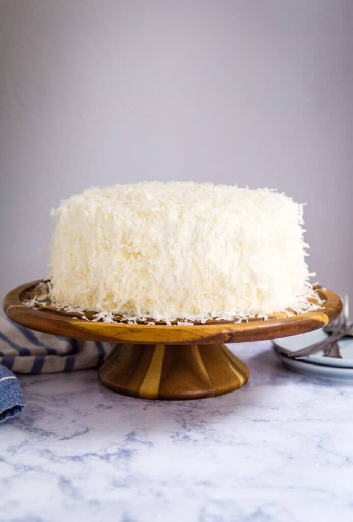 A white cake covered in coconut on a cake stand.