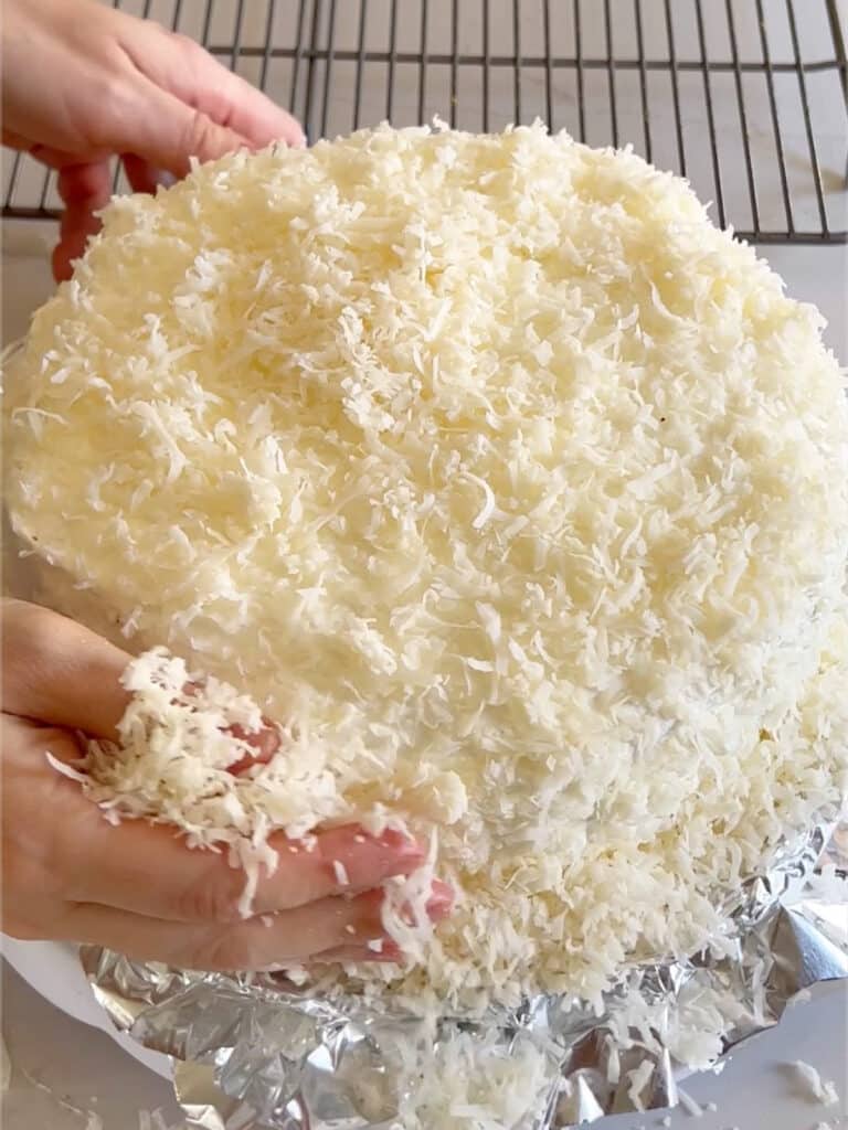 Hands patting coconut into a cake.