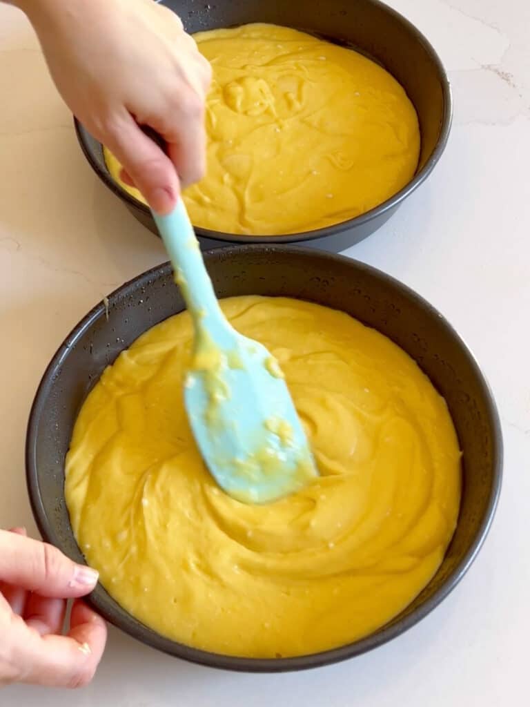 A spatula spreading cake batter into pans.