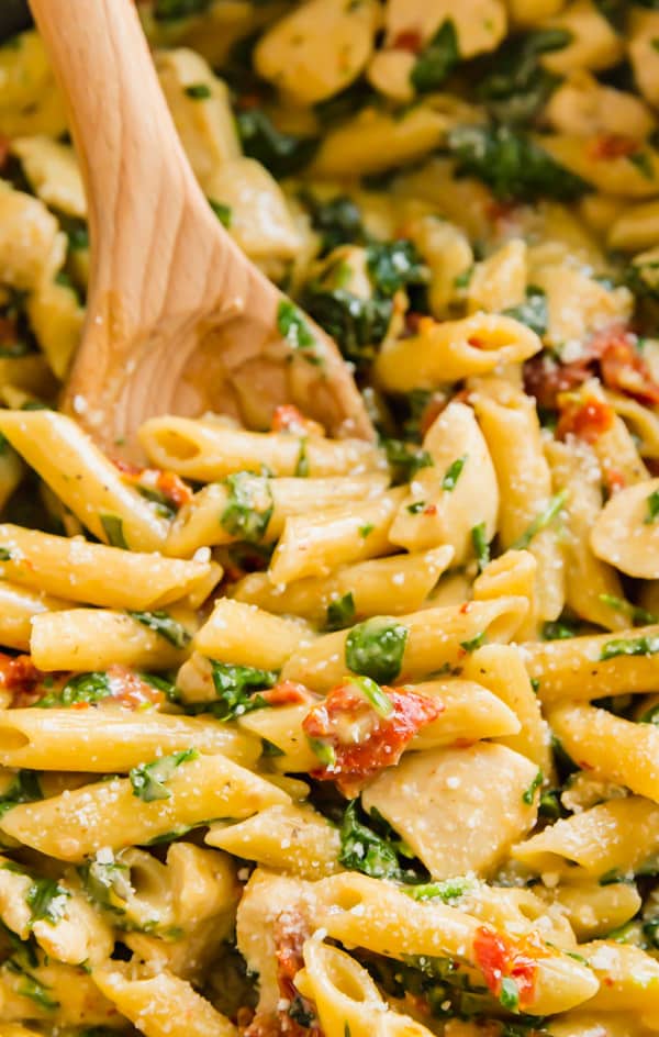 A close up image of chicken florentine pasta with a wooden spoon in it.