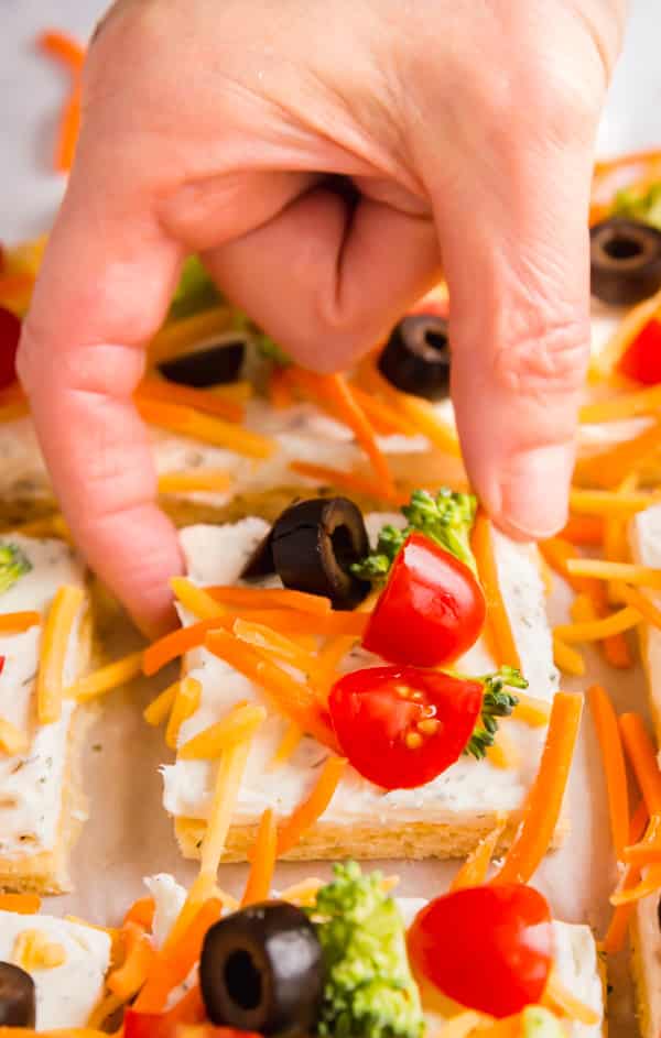 A hand reaching down and taking a piece of veggie pizza.