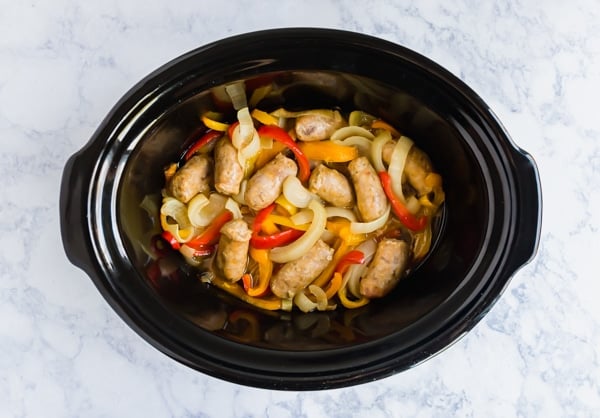An overhead image of sausage and peppers in a crock pot.