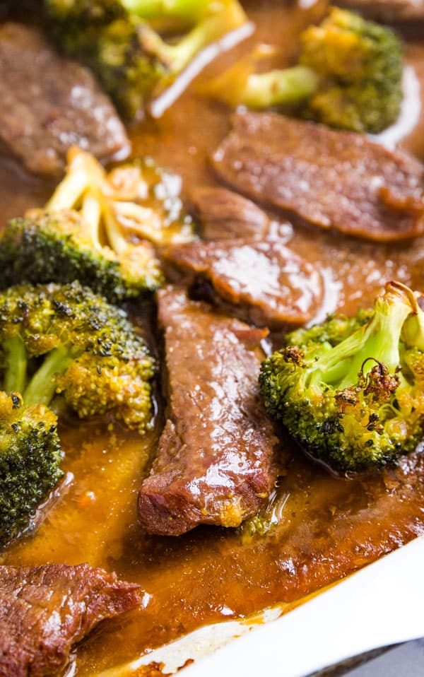 A close up image of a slice of beef on a pan surrounded by broccoli, sauce and other pieces of beef.