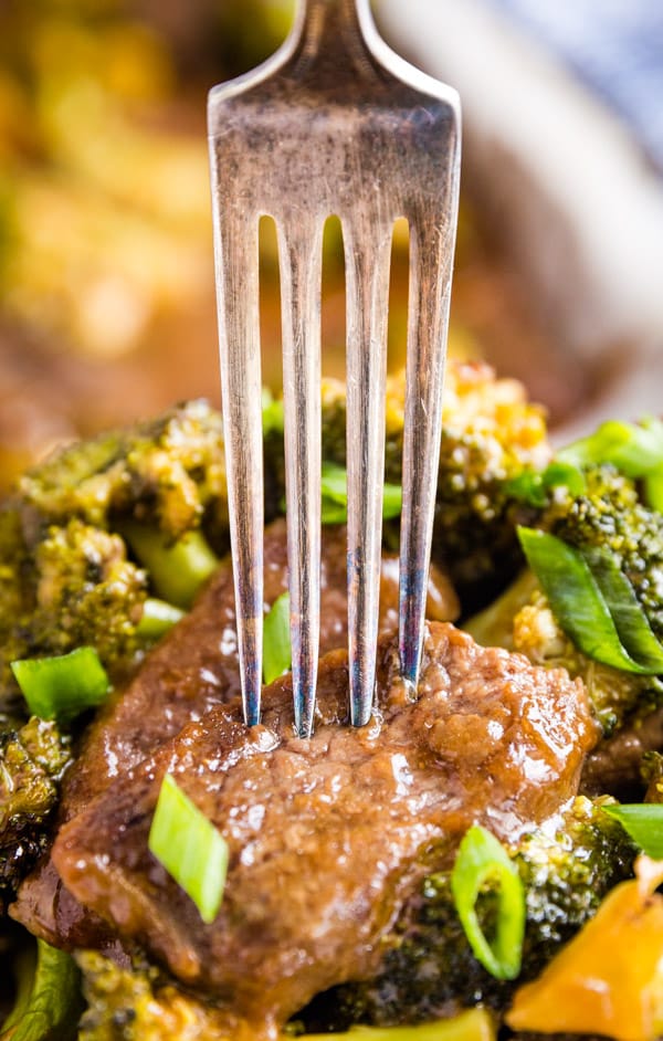 A fork piercing into a piece of beef with broccoli under it and the pan in the background.