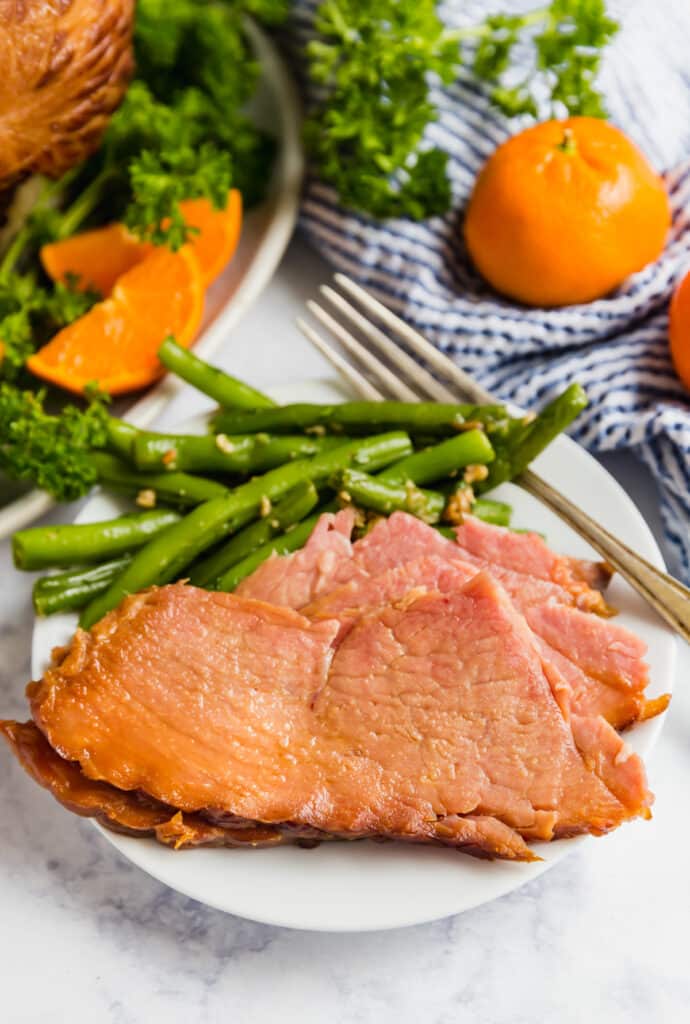 Sliced ham on a plate with green beans.