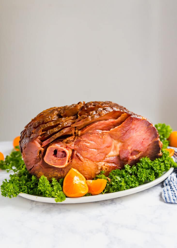 A straight on image of a spiral ham on a platter with oranges and parsley.