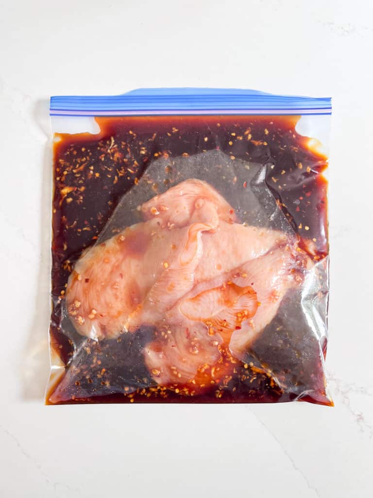 Raw chicken breast marinating in a plastic back.