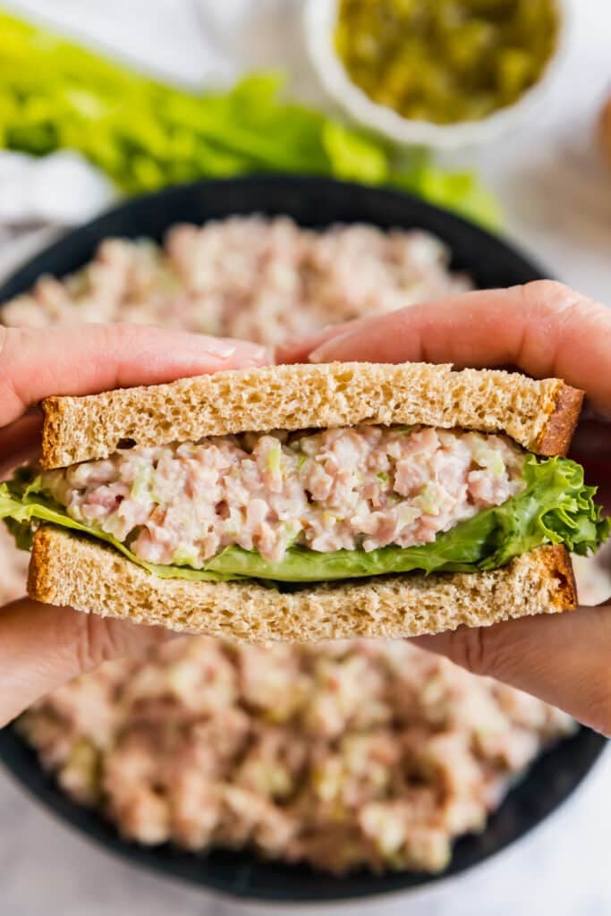 Hands holding up a half ham salad sandwich with the middle exposed to the camera.